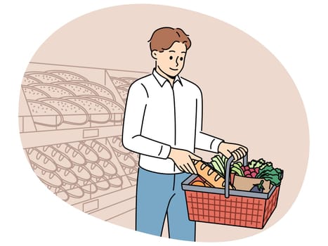 Man customer at grocery supermarket takes bread from shelf and puts it in basket of groceries. Guy visits supermarket or bakery buying fresh baguette and organic vegetables for preparing lunch.