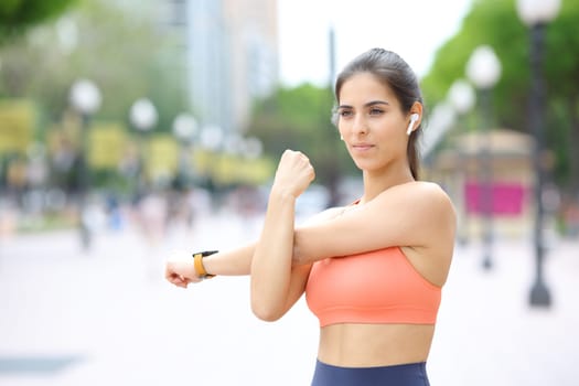 Runner wearing earphone listening to music stretching arms in the street