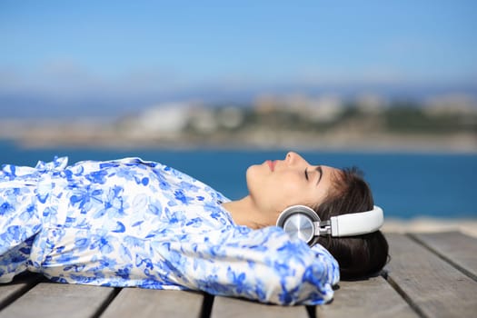 Profile of a woman resting listening music lying on a wooden platform on the beach