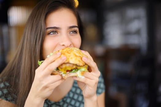 Happy woman eating hamburger in a restaurant interior looking away