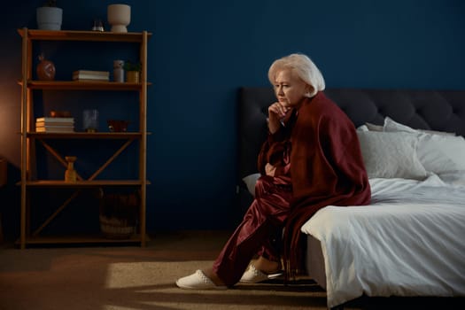Elderly woman wearing pajamas sitting on bed feeling loneliness having psychological and mental troubles