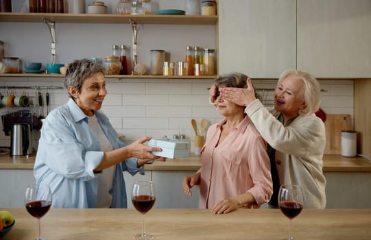 Happy elderly ladies at home kitchen. Two retired senior women preparing surprise gift for their friend. Friendship, bonding and birthday celebration