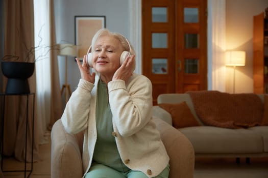 Grey-haired elderly woman in headphones listening to music. Leisure activity on retirement with modern technologies