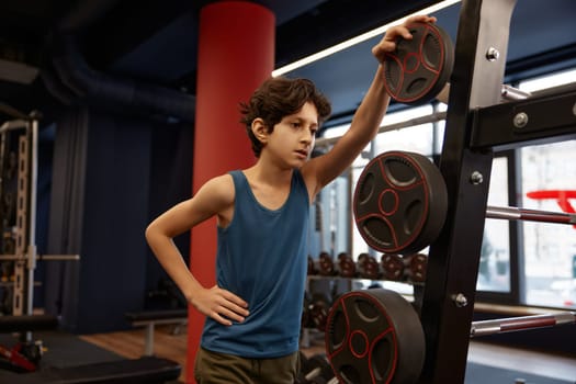 Tired preteen boy wiping sweat from his forehead with hand after training. Professional equipment for bodybuilding workout for children
