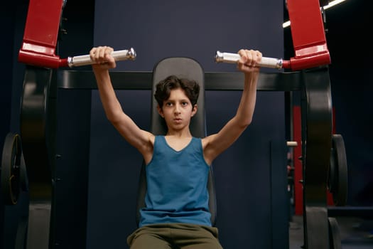 Active athletic preteen boy training arms muscles at gym. Children physical wellness, body and health care concept