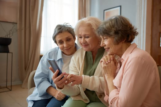 Smiling retired women looking on smartphone screen. Elderly ladies enjoying fun video or speaking online with their friends in social media. Female friendship community