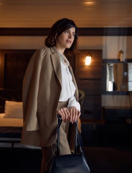 Elegant stylish businesswoman holding handbag over suitcase standing in luxury hotel room. Female entrepreneur during business trip