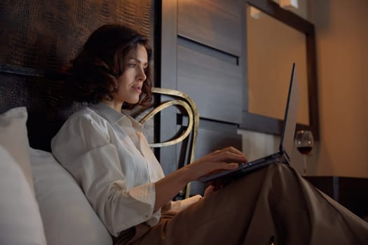 Businesswoman working online using laptop while resting with comfort and tranquility in bed at hotel room