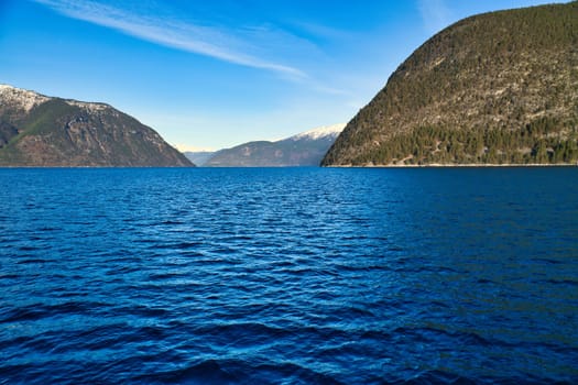 Norwegian fjord landscape. Blue water overlooking mountains with snow-covered peaks. Scandinavian nature from the north