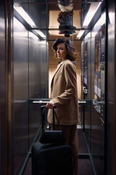 Elegant fashionable young businesswoman with luggage bags riding in hotel elevator arriving at place of destination. Business trip