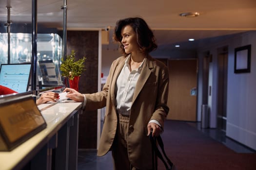 Young elegant businesswoman at hotel reception taking key from room. Female business traveler getting professional service