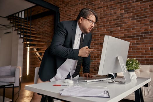 Mad furious businessman screaming loudly on computer screen while having online business meeting at home office. Remote job, videoconference, troubles at work, pc problems