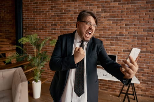 Crazy boss mad businessman shouting on mobile phone having bad conversation with employee or coworker. Angry male entrepreneur working remotely feeling displeasure
