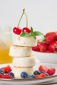 A stack of four cheesecakes on a plate with berries, blueberries, strawberries and cherries. Background white