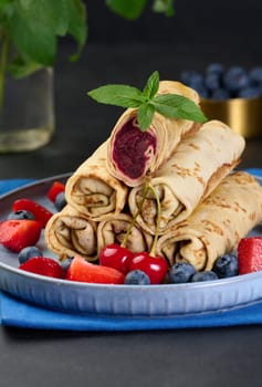 Crepes stacked in a pile, one of which is cut and filled with berry filling. The plate is also decorated with blueberries, black background