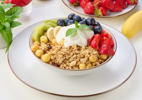 Granola with strawberries, kiwi, banana and blueberries in a round plate topped with yogurt on the table. Healthy and tasty food