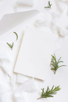 Blank card near white silk ribbons and rosemary leaves top view, wedding mockup. Romantic scene with vertical cards and aromatic leaves flat lay. Valentines, Spring or Mothers day concept