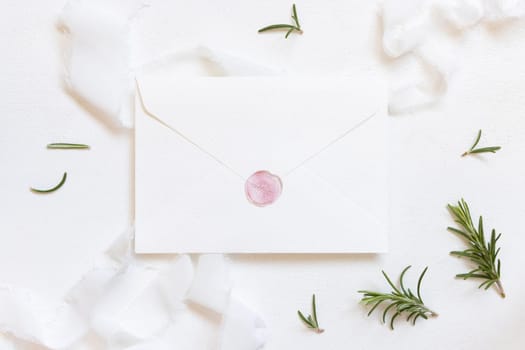 Blank sealed envelope near white silk ribbons and rosemary leaves top view, wedding mockup. Romantic scene with vertical cards and aromatic leaves flat lay. Valentines, Spring or Mothers day concept