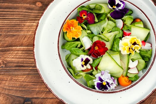 Salad made from fresh vegetables and decorated with edible flowers on rustic table. Copy space. Space for text.