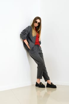 Young woman in casual sportive clothes with her hands in pockets leaning against white wall