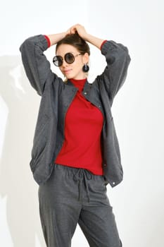 Young woman in grey cotton tracksuit, red turtleneck and sunglasses lifting hands