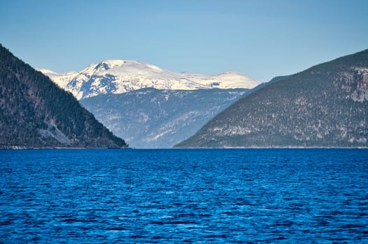 Norwegian fjord landscape. Blue water overlooking mountains with snow-covered peaks. Scandinavian nature from the north