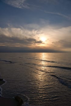 Sunset, illuminated sea. Sandy beach in the foreground. Light waves. Baltic Sea. Landscape on the coast