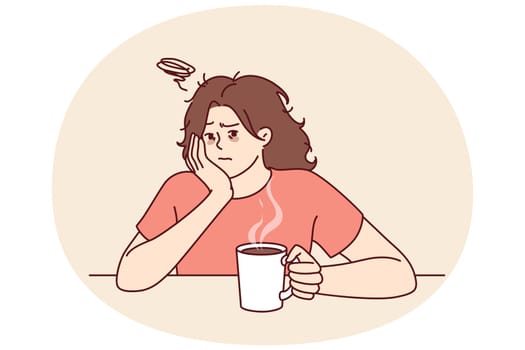 Tired woman with sad face drinks hot coffee and does not want to go to work due to lack of sleep. Upset girl is sitting at table with mug of coffee on Monday morning and is sad because weekend is over