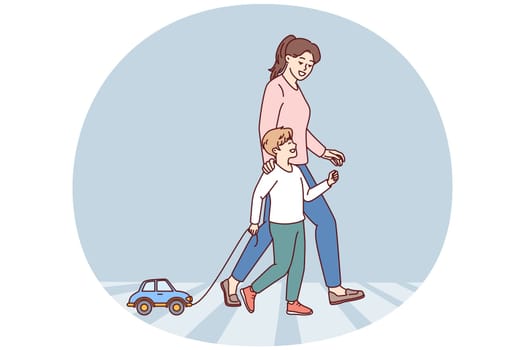 Happy mom and child going along pedestrian crossing across road walking through summer city. Little boy with toy car walks with nanny teaching how to cross intersection road correctly
