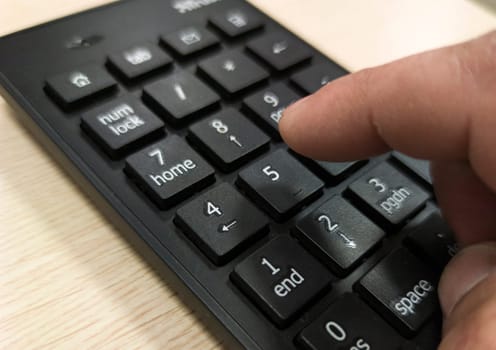 Mature mans hand pressing a numeric keypad. Wooden surface