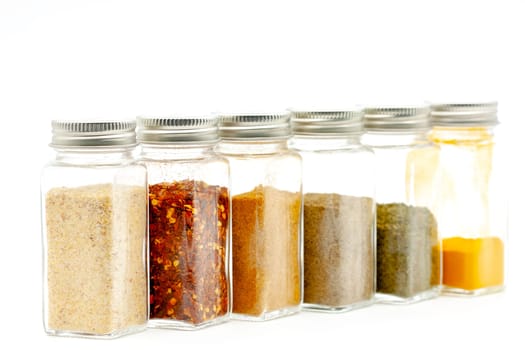 Square glass jars for storing dry kitchen spices. Selective focus with shallow depth of field.