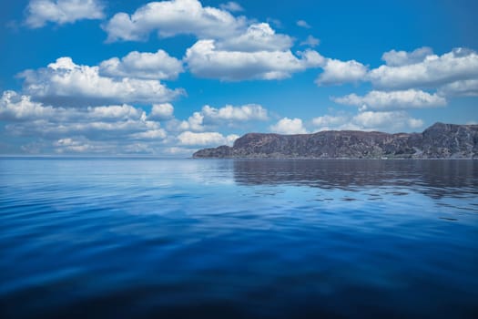 View from the sea to the West Cape in Norway in sunshine with white clouds. Waves in the foreground, rocks in the background. Westernmost point of the Eu
