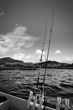 Fishing boat with fishing rod off mountains in the Norwegian fjord landscape in black and white. Crystal clear water in Scandinavia
