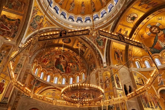 The big golden Chandelier inside of the Church of Saint, St. Sava, golden walls, vaults, ceiling covered in mosaics in the background, Belgrade, Serbia 2022