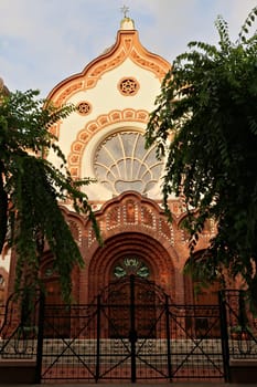 The front facade, entrance of the Synagogue of Subotica, bordered by trees and illuminated by the sun at golden hour, Subotica, Serbia 2022