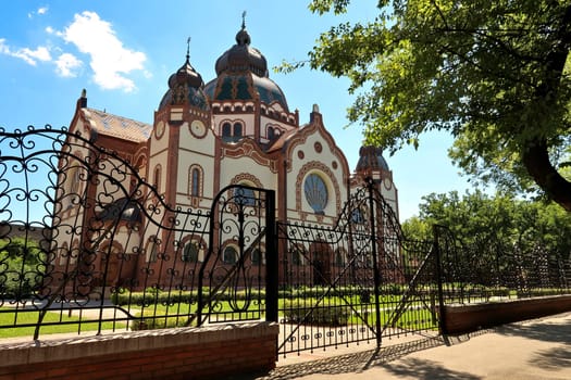 View onto the Synagogue of Subotica behind a black metal fence with elaborate details on a sunny day, Subotica, Serbia 2022