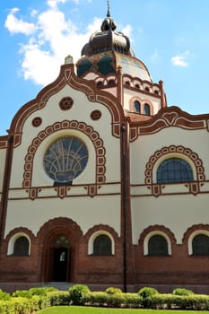 The side entrance and facade of the Synagogue of Subotica on a sunny day, some clouds are reflecting in the stained glass window, Subotica, Serbia 2022