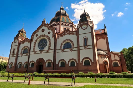 The entire facade around the side entrance of the Synagogue of Subotica on a sunny day, two little benches are standing in the foreground, Subotica, Serbia 2022
