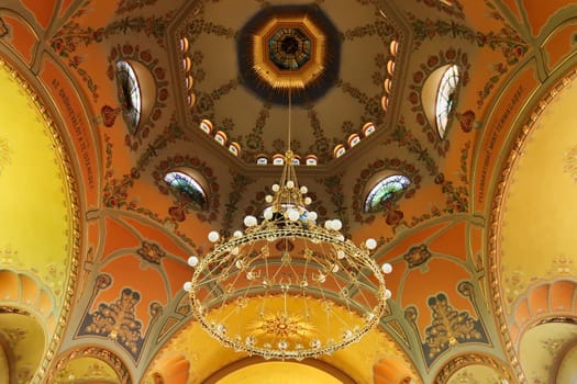 Inside the Synagogue of Subotica, the big golden chandelier is hanging from the ceiling, covered in colorful ceiling paintings, frescos, Subotica, Serbia 2022