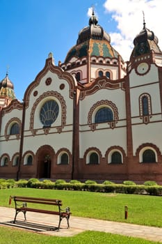 The side entrance and facade of the Synagogue of Subotica on a sunny day with a little bench in the foreground, Subotica, Serbia 2022