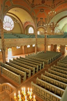 Inside the Synagogue of Subotica, a golden chandelier is hanging from the ceiling over the benches and the aisle, candles are burning in the foreground, Subotica, Serbia 2022