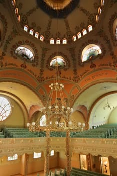 Inside the Synagogue of Subotica, the golden chandelier is hanging from the painted ceiling, vault, dome, light is shining through stained glass windows in the background, Subotica, Serbia 2022
