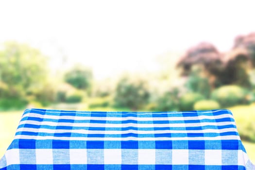 Empty table product. Empty colorful checkered tablecloth over abstract blurred natural green background texture with space for food and product display montage.