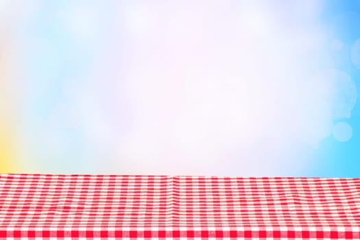 Empty table product. Empty colorful checkered tablecloth over abstract blurred natural spring background texture with space for your food and product display montage.