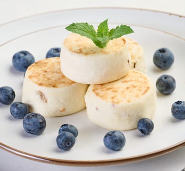Round small fried cheesecakes on a plate with blueberries. Background white