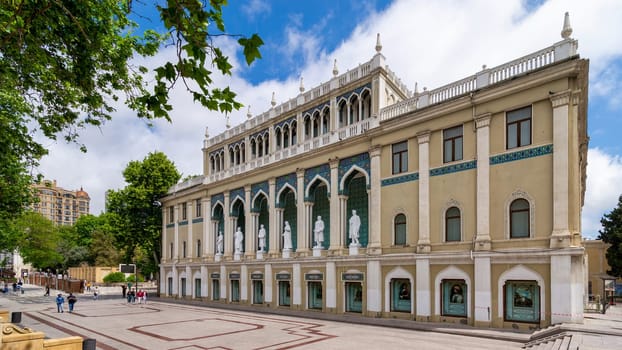 Baku, Azerbaijan - May 5, 2024: Nizami Museum of Azerbaijan, with statues lining the facade. The building is decorated with arches and intricate tile work. People can be seen walking near the building