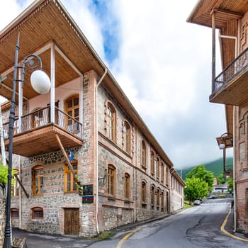 A view of a traditional stone bricks building with a wooden balcony, located on a narrow street in Sheki, Azerbaijan