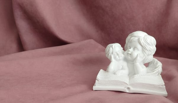 A plaster statuette of two white angels reading a large book.Texture or background.