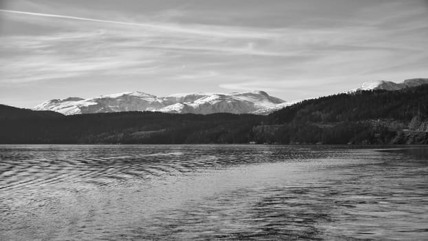Norwegian fjord landscape in black and white. Blue water view of mountains with snow-covered peaks. Scandinavian nature from the north