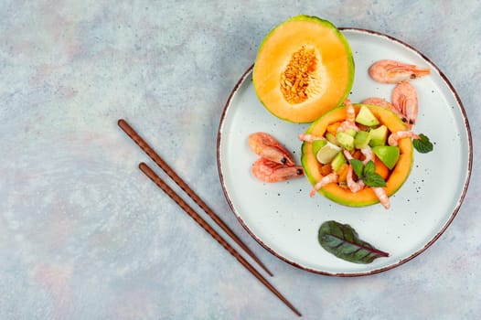 Delicious Asian salad of melon, shrimp and avocado in a half of melon on wooden table.